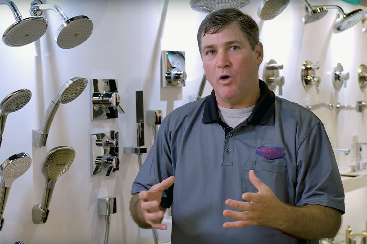 Plumber standing in front of showerheads, giving lesson about them.
